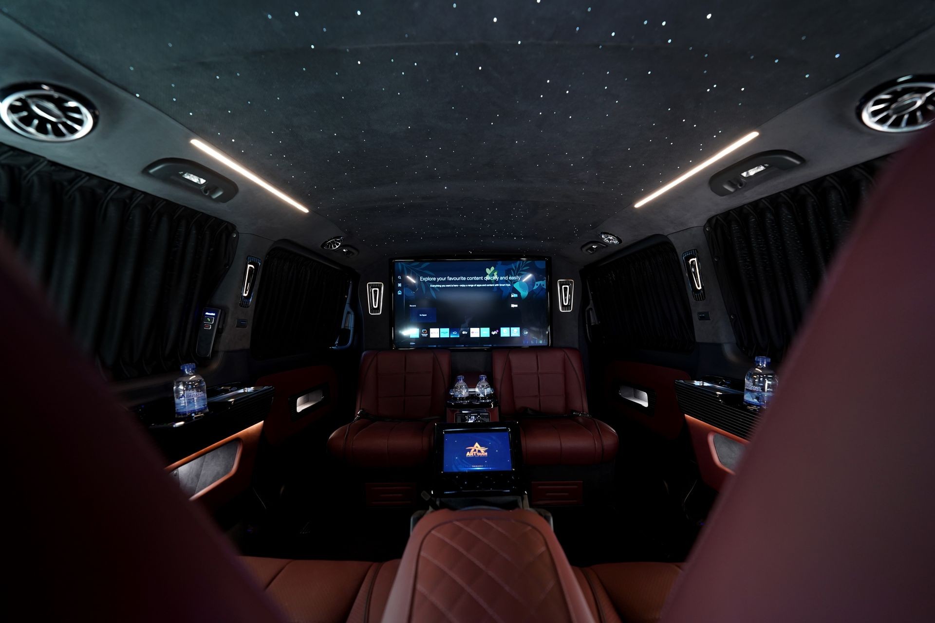 Luxurious vehicle interior with leather seats, ambient lighting, and a large screen at the front.