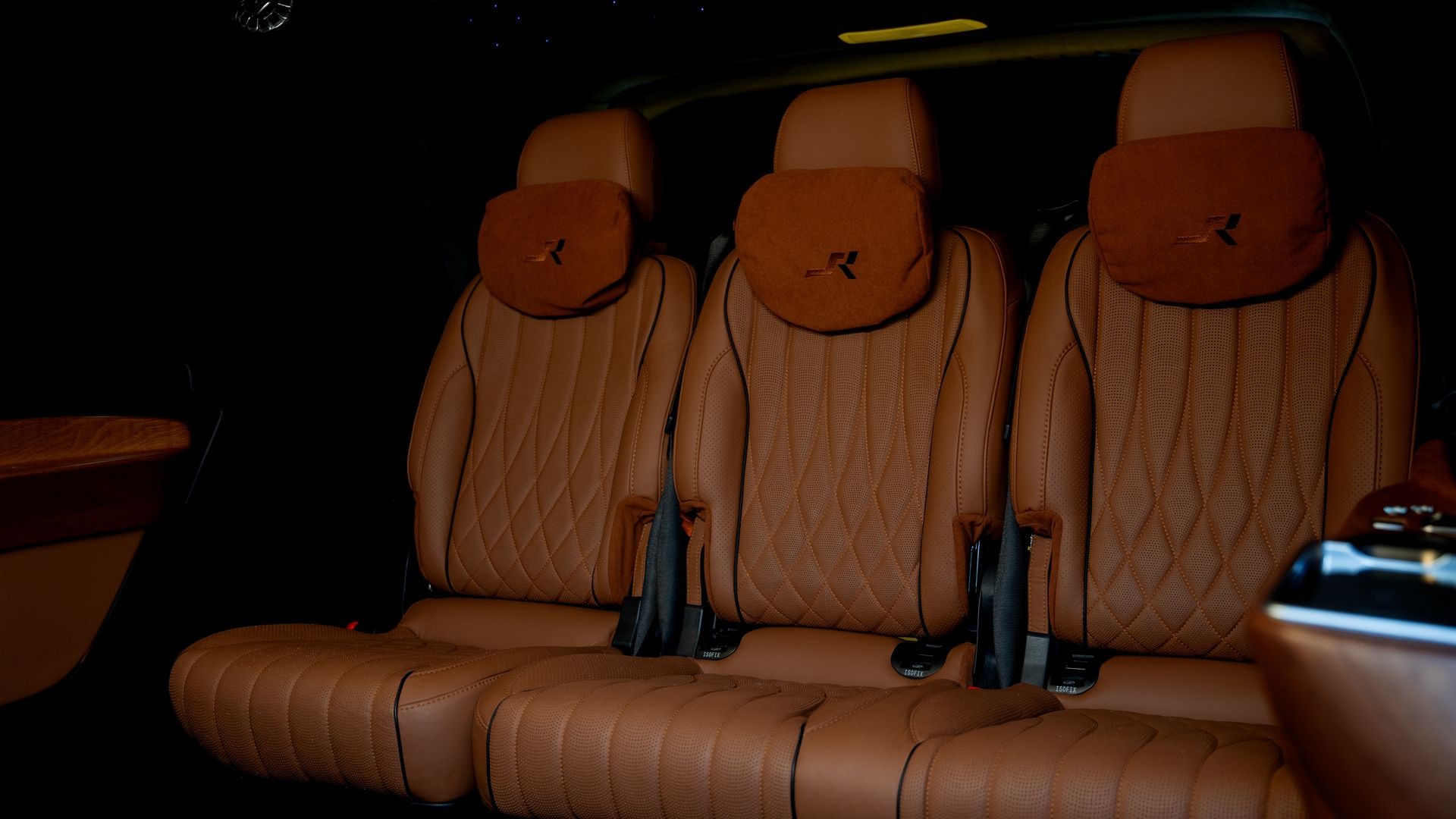 Luxury car interior with three brown leather seats, quilted stitching, and adjustable headrests.